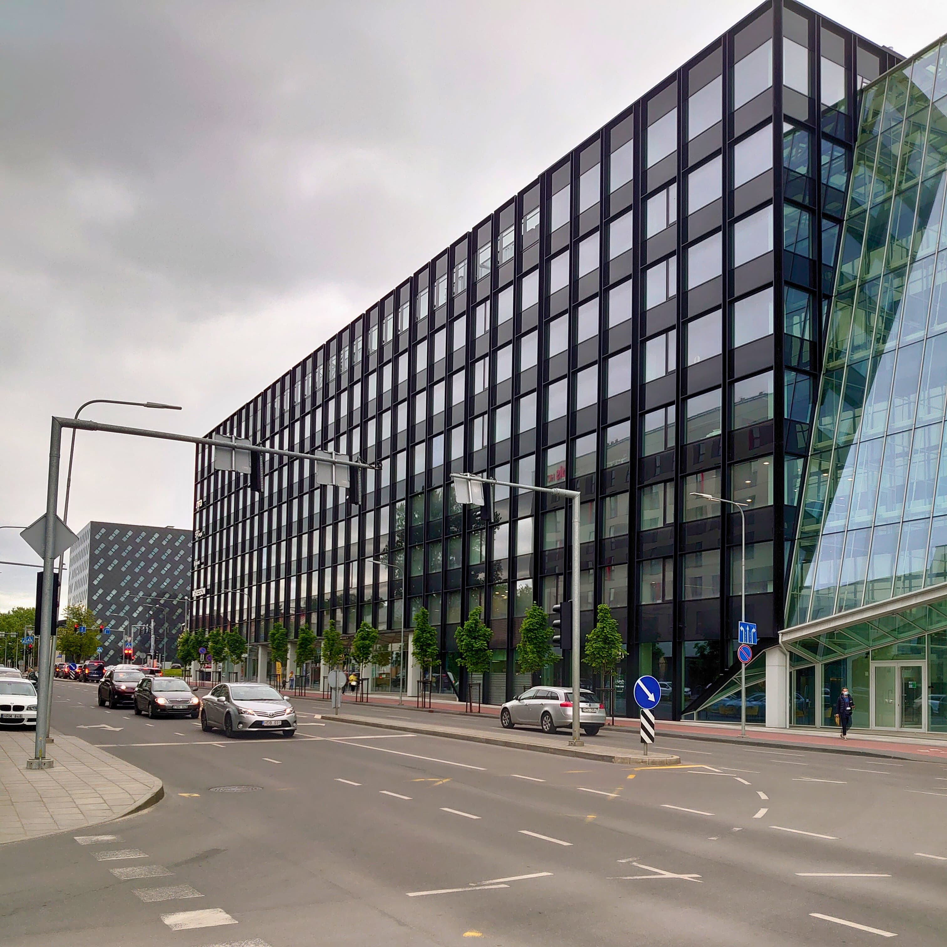 Šiuolaikinis verslo centras su stikliniais langais, esantis šalia kelio, atspindintis statybos įmonės fasado montavimo darbus.