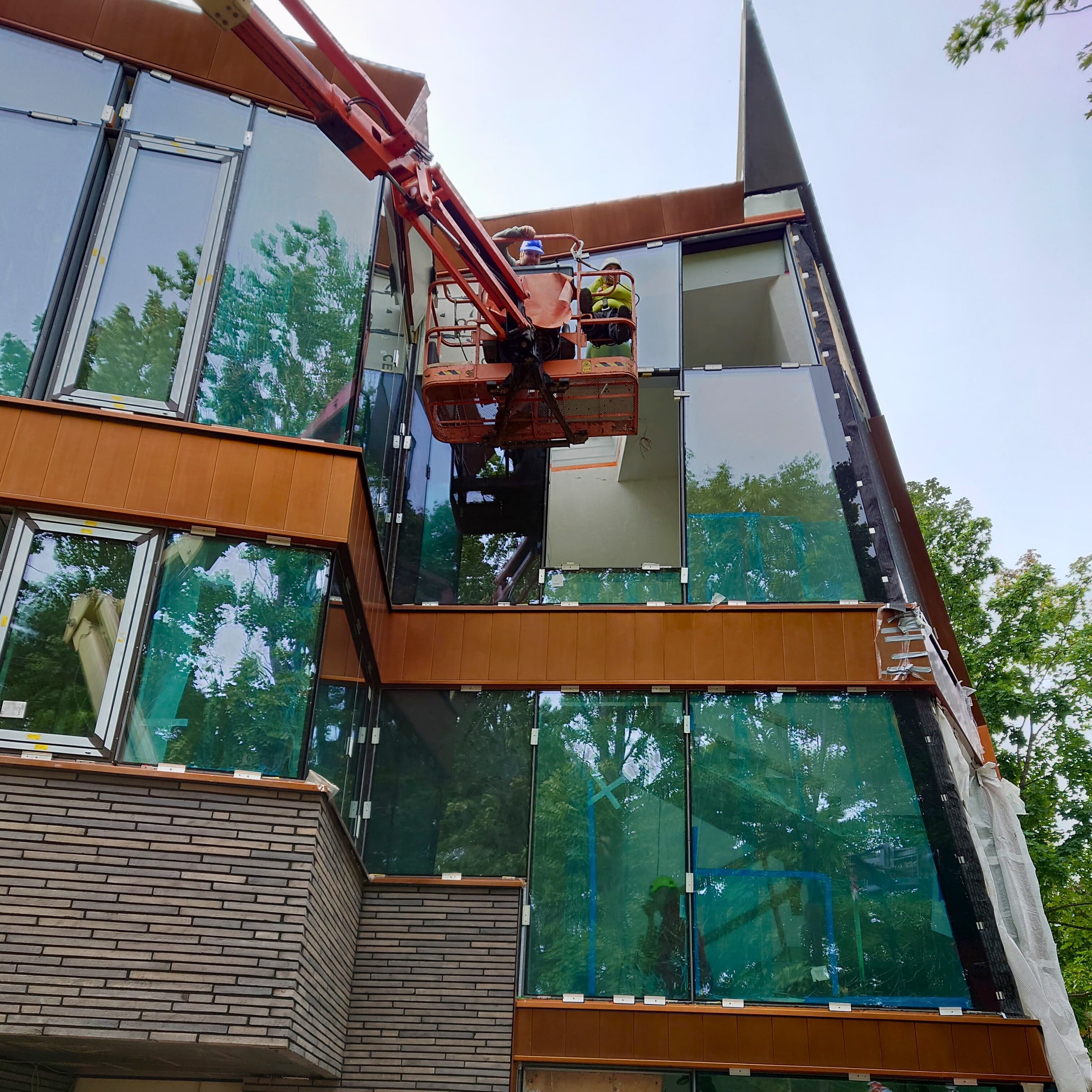 Statybos įmonės darbuotojas montuoja stiklo langus pastate, pabrėždamas statybos procesą.