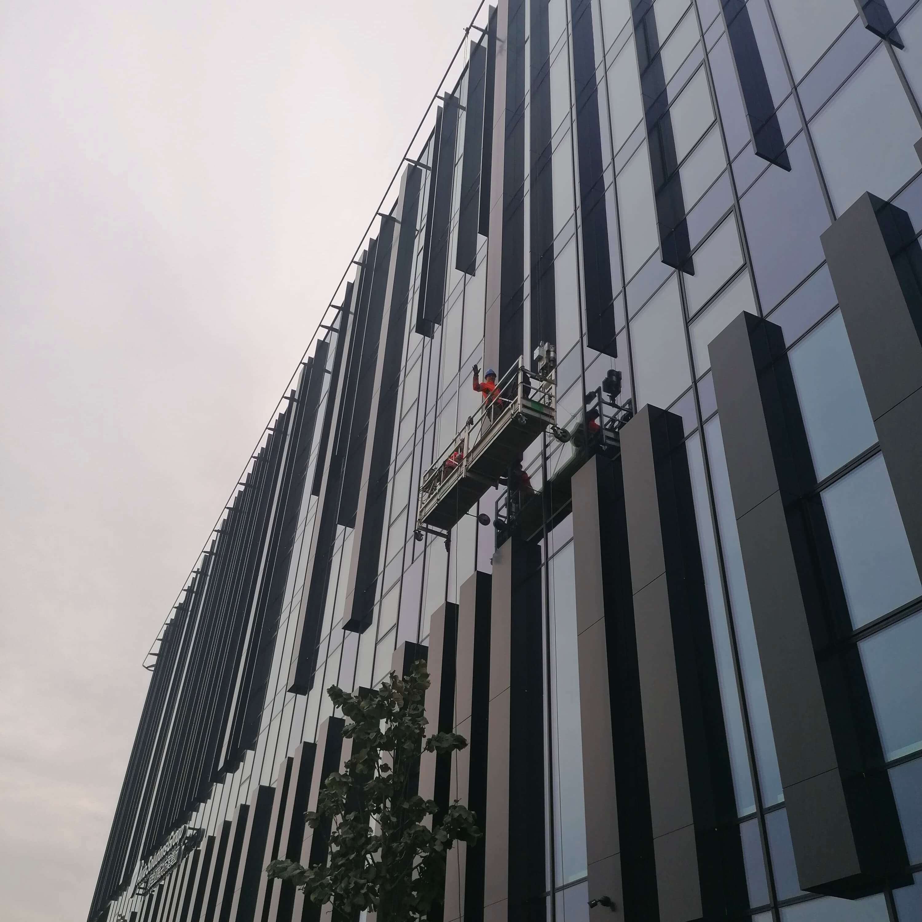 Vyras ant kopėčių dirba prie pastato, naudodamasis kėlimo platforma geresniam priėjimui ir stabilumui užtikrinti.