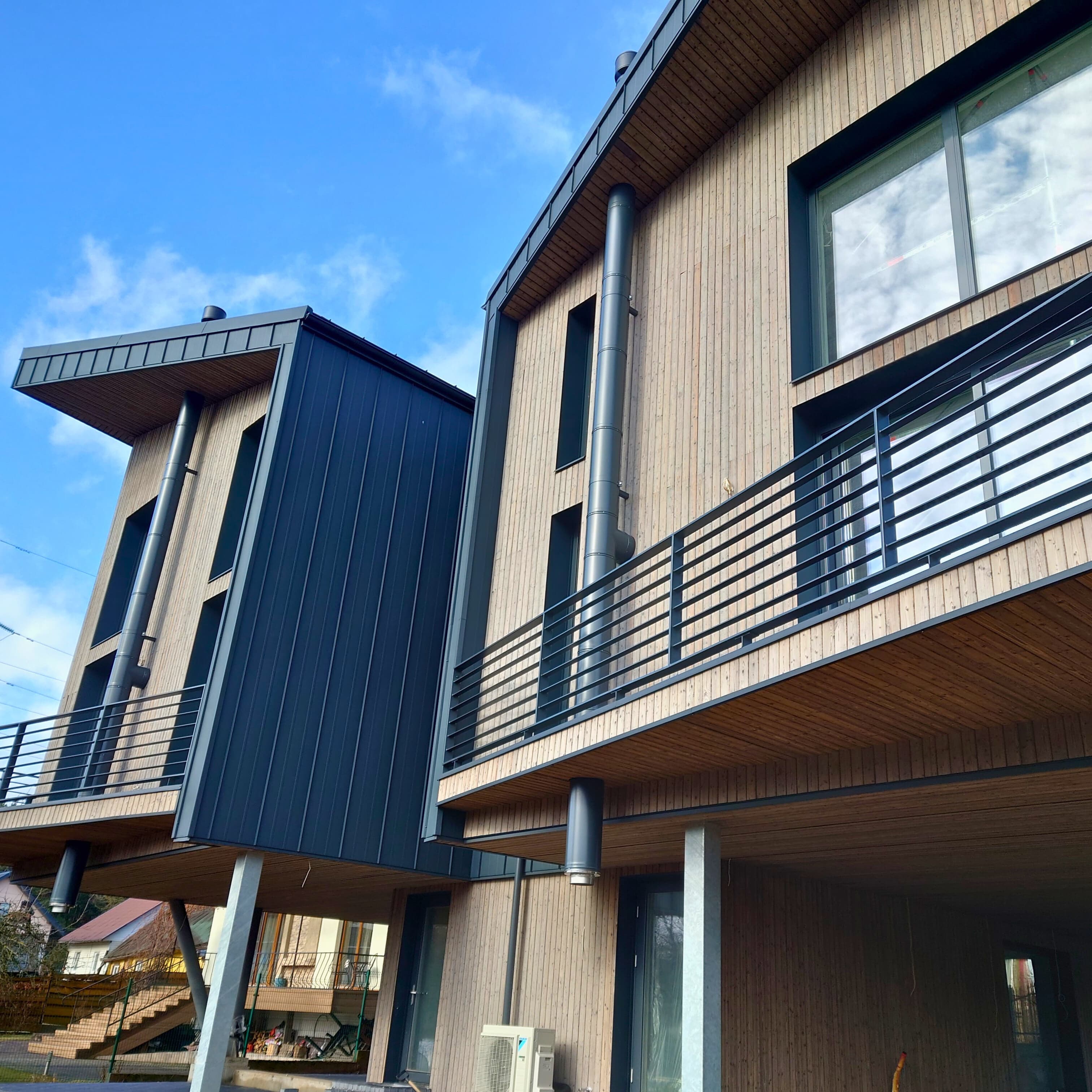 Du šiuolaikiniai mediniai namai su balkonais ir stikliniais fasadais, atspindintys pirmaujančią statybos įmonę Lietuvoje.